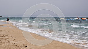 Woman walking in the sandy beach a View from the back. Stormy weather on the sea coast. Stormy summer day.