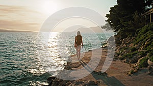 Woman walking by the sea at sunset. A tourist strolling along the coastal path with the sun reflecting off the Adriatic