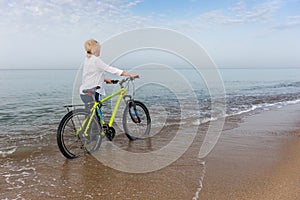 Woman walking in the sea wheeling a bicycle