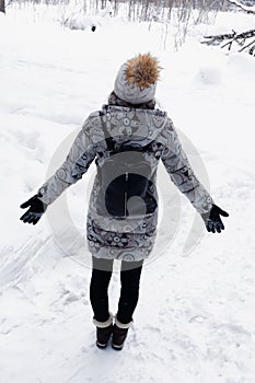 Woman walking in snow in winter clothes. Rear view of girl walking in snowy forest