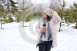 Woman walking on a snowy path in winter with a cup of drink in a forest setting