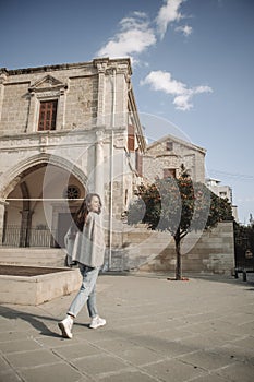 Woman is walking at the square with ancient building and tangerine tree