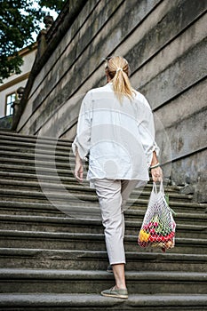 Woman walking at stairs and carrying mesh bag after shopping food in city