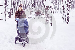 Woman walking with stroller in forest at winter.