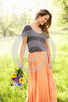 Woman Walking In Summer Field Carrying Flowers