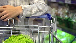 Woman walking in supermarket with shopping trolley, groceries shopping concept