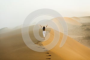 Woman walking on top of huge sand dune in Sahara desert. View from behind