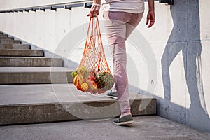 Woman walking up stairs and carrying reusable mesh bag after shopping food