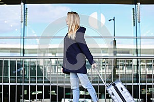 Woman walking with valise and wearing coat.