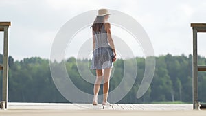 Woman walking on wooden pier. Having fun on summer day on the vacations. Young girl looking at water from the dock