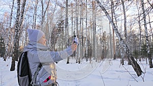 Woman is walking in the woods. Traveler is photographed on the phone in forest. Girl does selfie and communicates with