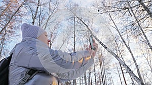 Woman is walking in the woods. Traveler is photographed on the phone in forest. Girl does selfie and communicates with