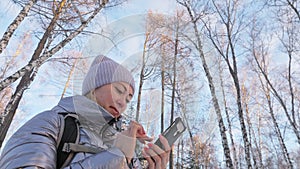 Woman is walking in the woods. Traveler is photographed on the phone in forest. Girl does selfie and communicates with