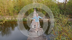 A woman walks across a flimsy suspension bridge over a river, overcoming her fear