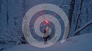 Woman walks alone in snowy forest holding burning torch to illuminate path through snowdrift at dusk