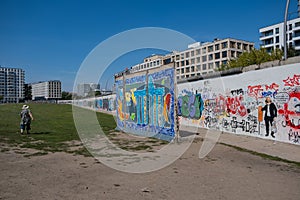 A woman walks along East Side Gallery, Berlin Wallin in front of modern buildings, Berlin, Germany