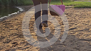 Woman walks along lake shore with vintage picnic basket