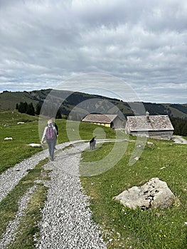 woman walks along a path in the mountains with a black dog