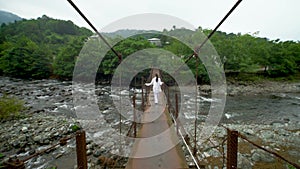 A woman walks along a suspension bridge over a mountain river.