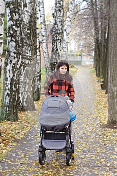 Woman walks in autumn park with baby buggy