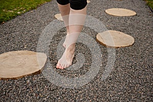 Woman walks barefoot along a tactile massage path made of small stones in the park. Concept of foot massage, meditation