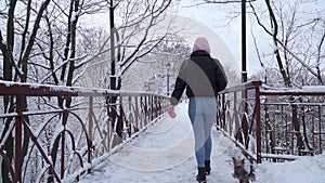 Woman walks on bridge with her dog on leash. Small yorkshire terrier runs near owner on snow. Slow motion.