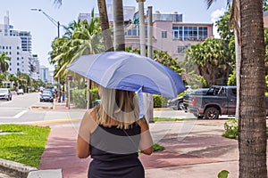 Woman walks down street, shielding herself from scorching sun with UV-protective umbrella.