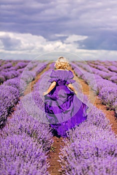 A woman walks in a field of lavender. A girl in a purple dress runs in lavender. Photo from the back