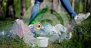 A woman walks past a pile of garbage in the forest and throws a glass bottle at it