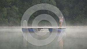 Woman walks on pontoon in lake in morning mist