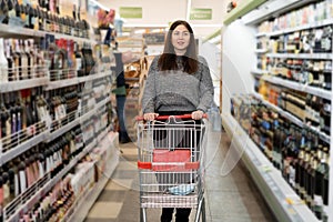 A woman walks with a shopping trolley in a supermarket past the shelves with groceries. Shopping in a large store.