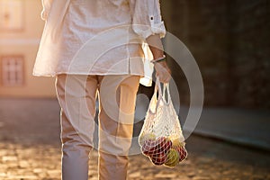 Woman walks on street and carrying reusable mesh bag with apples