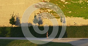 Woman walks in summer park with sheared bushes