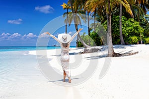 Woman walks on a tropical beach with white hat