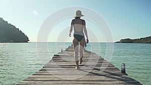 Woman walks on wooden jetty on tropical beach