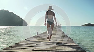 Woman walks on wooden jetty on tropical beach