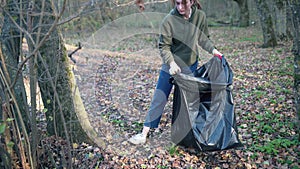 A woman walks through the woods and removes plastic bottles. Garbage bag to clean the environment from pollution