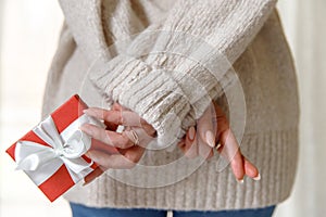 Woman wants to give a gift surprise in a red box to her boyfriend and worried, crossed her fingers, view from back