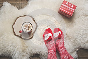 Woman in warm christmas knitted socks wants to drink coffee and open a gift. Top view.