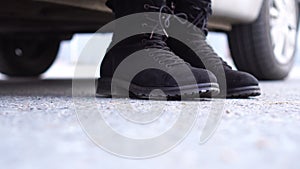 Woman in warm clothes getting out of car, legs in boots close-up on road in city. Low angle shot