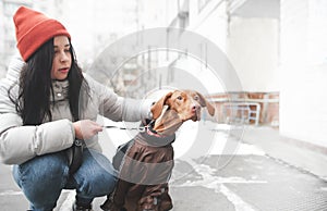 Woman in warm clothes holds on a leash an amusing dog surprised eyes looking to the side