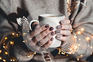 A woman in warm clothes of neutral tones with a Christmas garland. matte stylish manicure. gel polish.