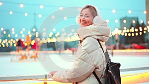 Woman in warm clothes smiling at camera outside ice rink during Christmas