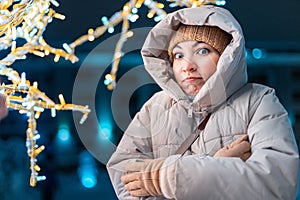 Woman in a warm down jacket and thermal underwear is frozen and shivering during a severe frost while walking around the New