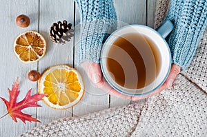 Woman in a warm knit sweater holds a cup of tea in hands on a wooden table