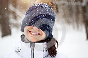 A woman with a warm knitted hat pulled over her eyes smiles and enjoys the snow, the spring sun. Outdoor activities, seasonality,