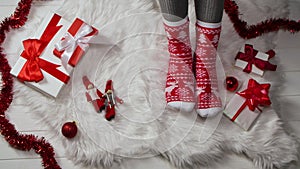 Woman in warm red white socks with an ornament sits on a fur skin around boxes with gifts and New Years decorations