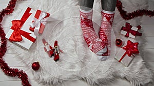 Woman in warm red white socks with an ornament sits on a fur skin around boxes with gifts and New Years decorations
