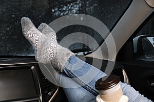 Woman in warm socks with coffee resting inside car