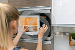 Woman warm up the food in microwave oven at home